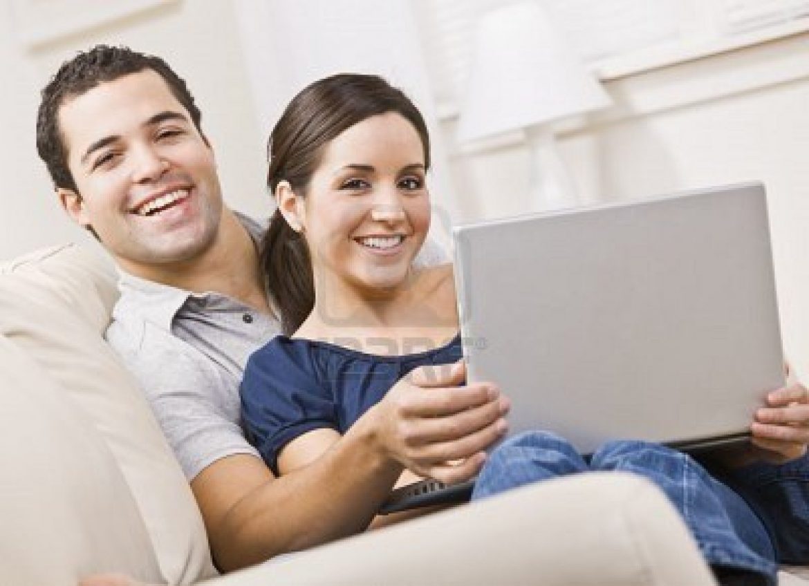 5120713-an-attractive-young-couple-sitting-on-a-couch-together-and-holding-a-laptop–they-are-smiling-direct